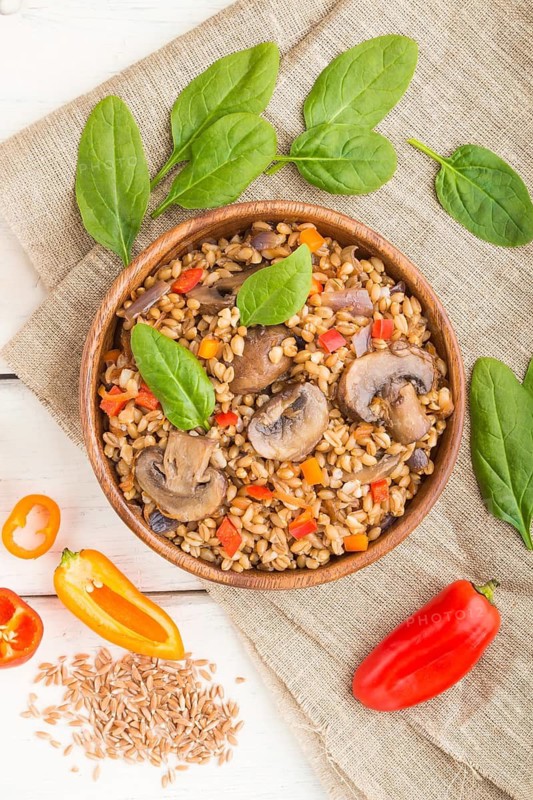 Spelt (dinkel wheat) porridge with vegetables and mushrooms in wooden bowl on a white wooden background and linen textile. Top view, flat lay, copy space. Russian traditional cuisine
