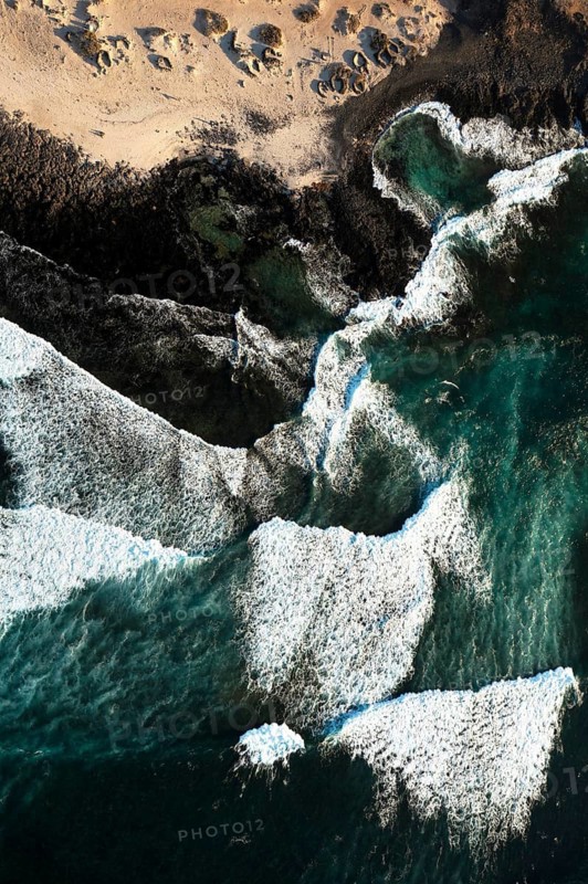 Aerial view of frothy ocean waves meeting the distinct rocky shores of Popcorn Beach in Fuerteventura, showcasing the powerful natural beauty