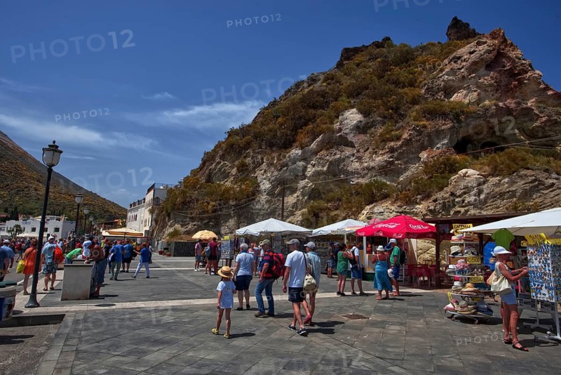 A lively square with tourists and colorful umbrellas against a rocky backdrop, Vulcano Lipari Islands, Sicily Italy