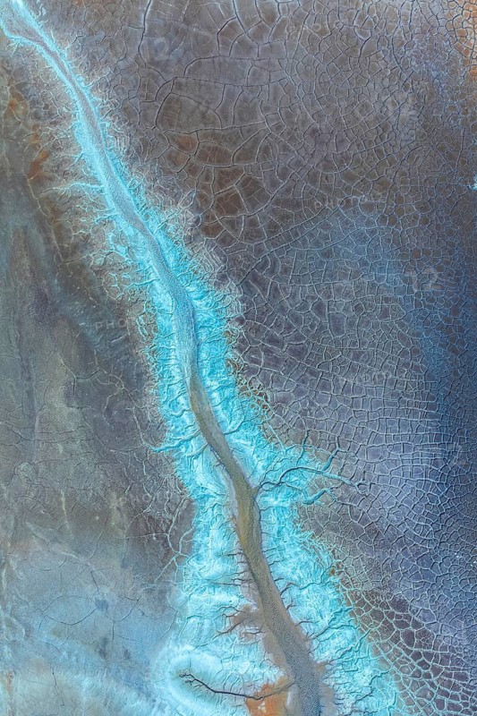 A mesmerizing aerial view of an abstract cracked landscape pattern, featuring intricate blue and earth-toned textures. The scene evokes a sense of natural artistry