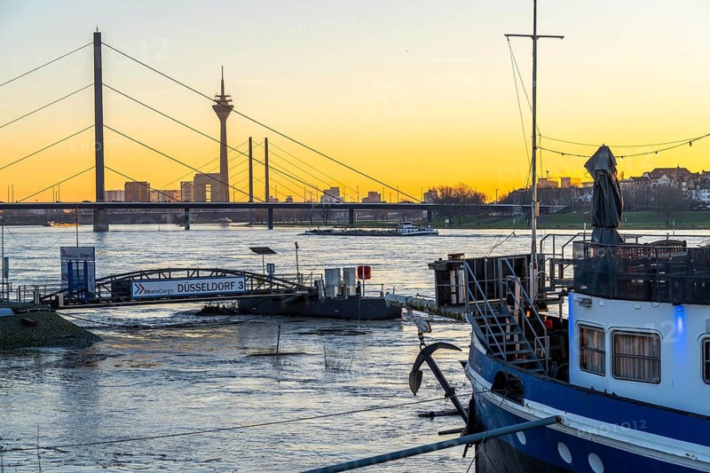 Sunset on the Rhine near Düsseldorf, skyline of the city centre with Rhine Tower, Rheinkniebrücke, behind, Oberkassler Brücke, landing stage at the Rheinterrassen, restaurant ship, cargo ship on the Rhine, North Rhine-Westphalia, Germany