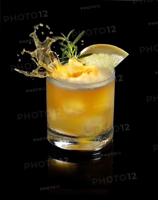 An ice cube cube falls into a tumbler and allows the liquid to splash on, studio shot against a black background