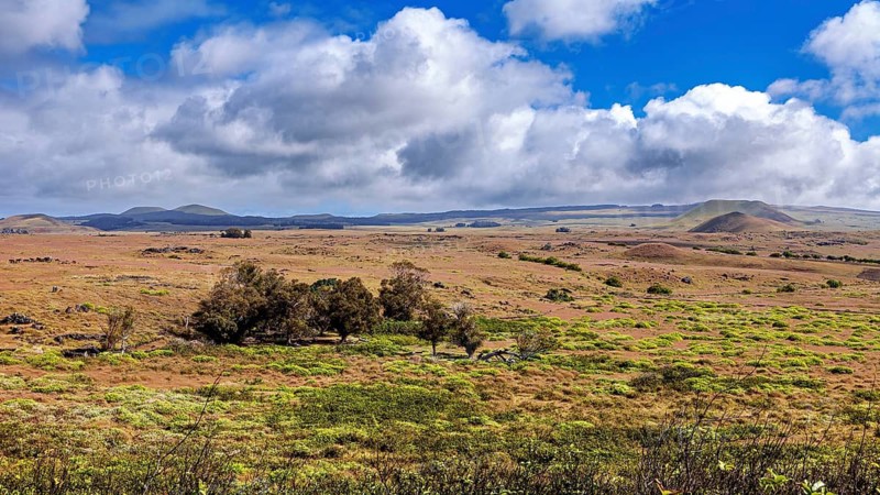 Wide grassland under dramatic sky with isolated green hills, the landscape of Easter Island in the Pacific Ocean