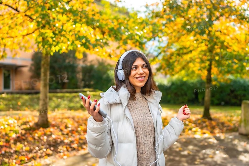 Caucasian beauty woman listening to music and dancing in the city park during a sunny day of autumn