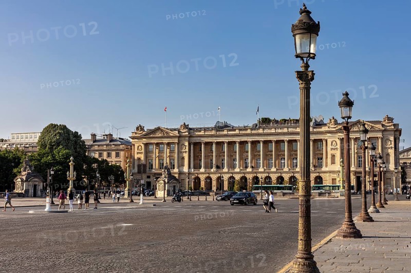 Elegant building on a large square, pedestrians stroll past, a few cars, Paris