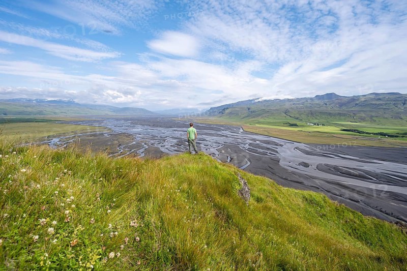 Hiker, young man on a hill, view over alluvial land, meandering river, Dímonarhellir, Suðurland, Iceland