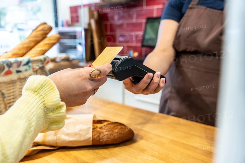 Customer holding a credit card over a payment terminal confirming a modern, convenient transaction for fresh bread at a small business counter, showcasing retail technology and tap to pay service