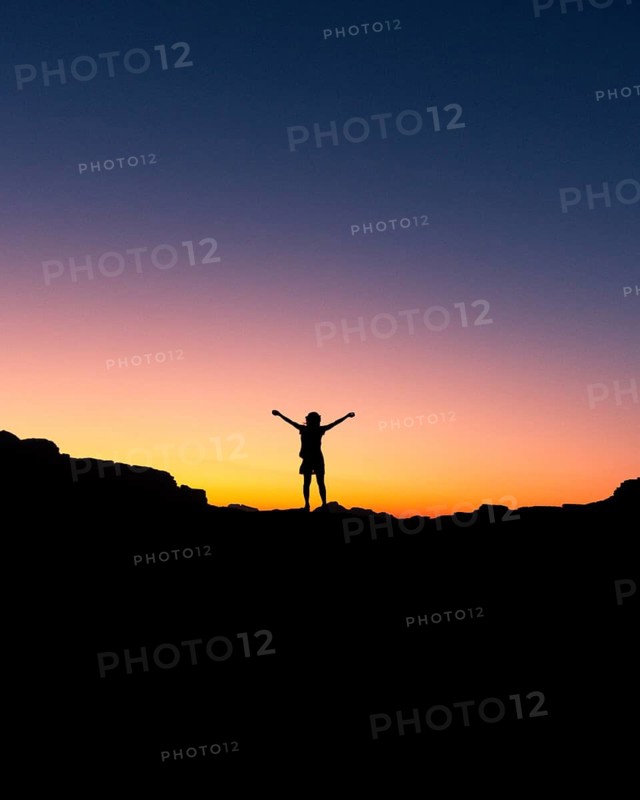 Happy celebrating winning success woman at sunset or sunrise standing elated with arms raised up in celebration of having reached mountain top summit goal during hiking travel trek