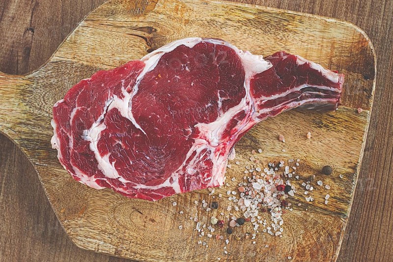 Raw rib eye steak, cowboy steak, on a wooden chopping board, top view, no people