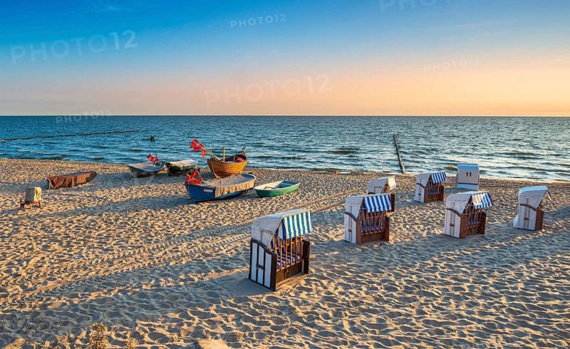 Beach chairs and fishing boats with red flags on fine sandy beach at sunrise, Baltic resort Kölpinsee, Usedom island, Mecklenburg-Western Pomerania, Germany