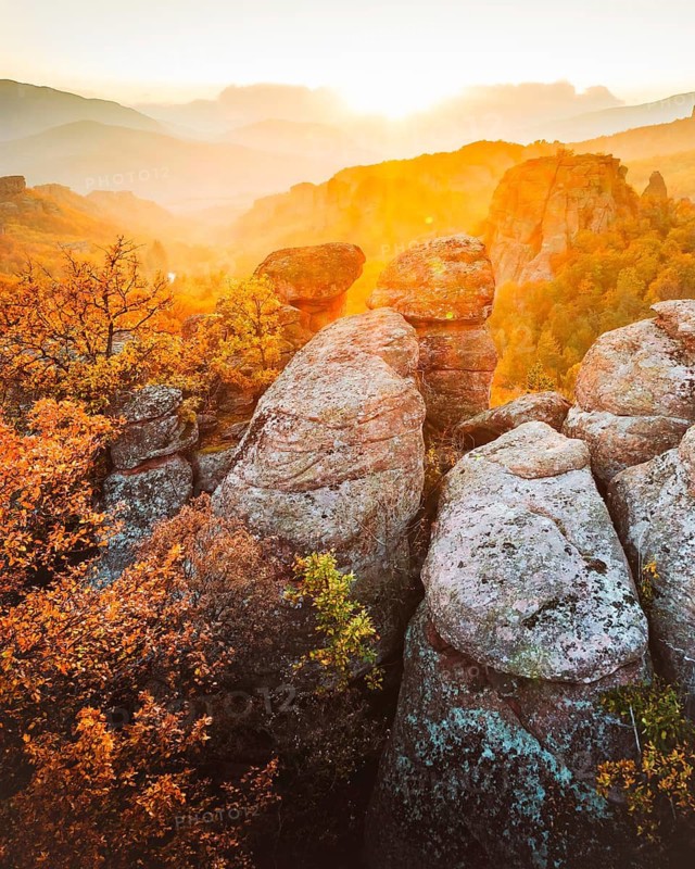 Dramatic aerial drone view over sandstone rock formations of Belogradchik in Bulgaria surrounded by autumn forest with vibrant foliage at golden sunset