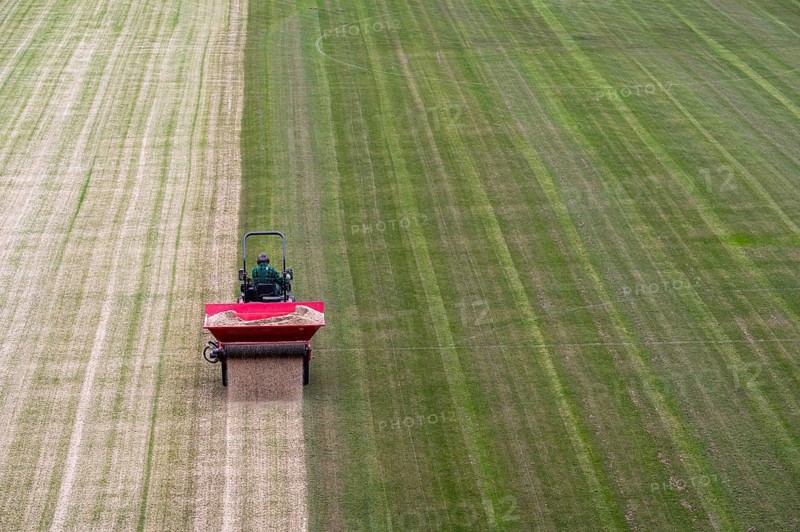 A worker in a tractor pours sand on a grass (top dressing) during the renovation of the soccer field in Lubin, Poland