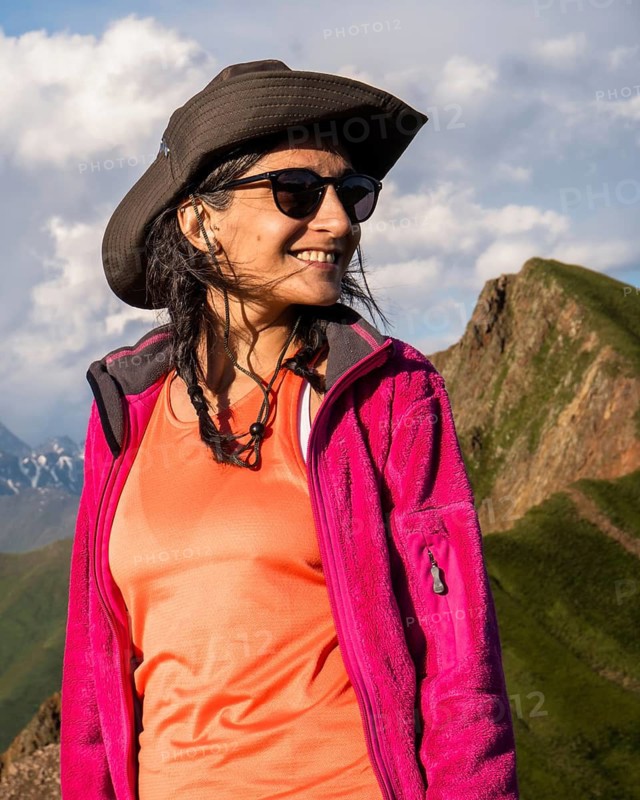 Happy Young Traveler hiker woman portrait wearing hat and jacket smiling in Kazbegi National Park mountains of Georgia, adventure lifestyle and hiking portrait