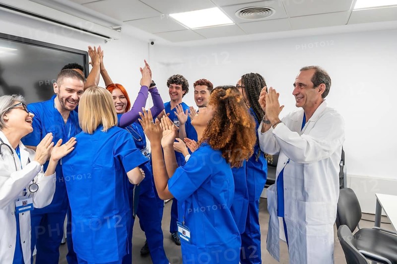 Medical team of diverse doctors and nurses clapping and offering high five gestures, showing unity, collaboration, and achievement in a hospital conference room setting