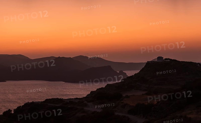 A captivating sunset over Milos Island, Greece, with the silhouette of hills and the vibrant orange sky reflecting on the Aegean Sea, creating a serene and picturesque scene
