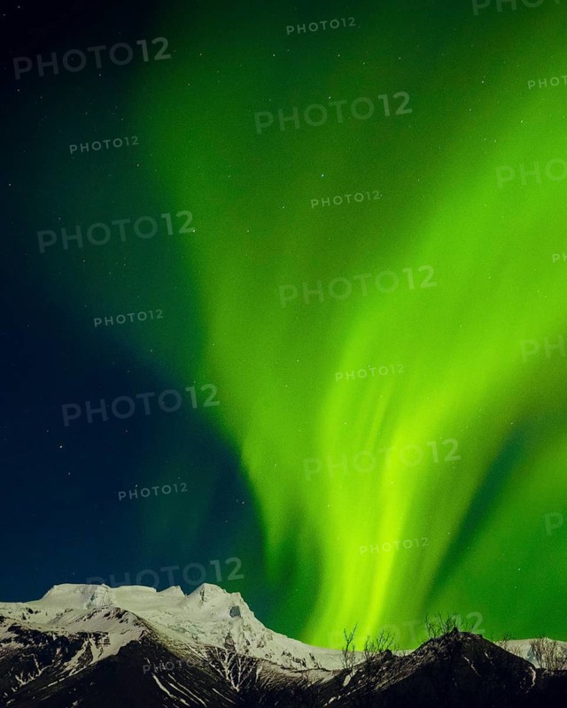 Brilliant green aurora borealis glowing above snowy mountain peaks under starry night sky, symbol of wilderness, beauty and protected national parks worldwide