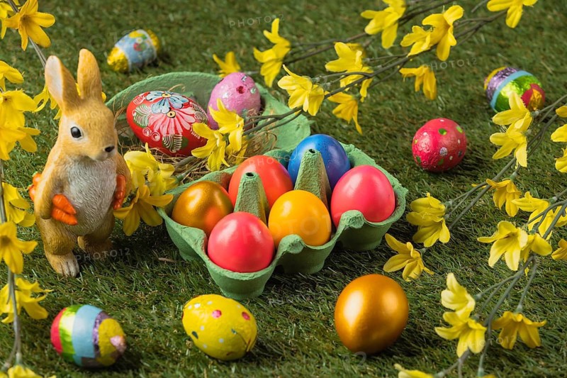 An Easter bunny figure next to colorful Easter eggs and bright blossoms on a green background