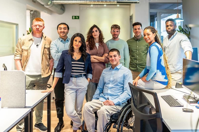 Multicultural team of professionals standing together in a modern office, showcasing diversity and inclusion with a colleague using a wheelchair