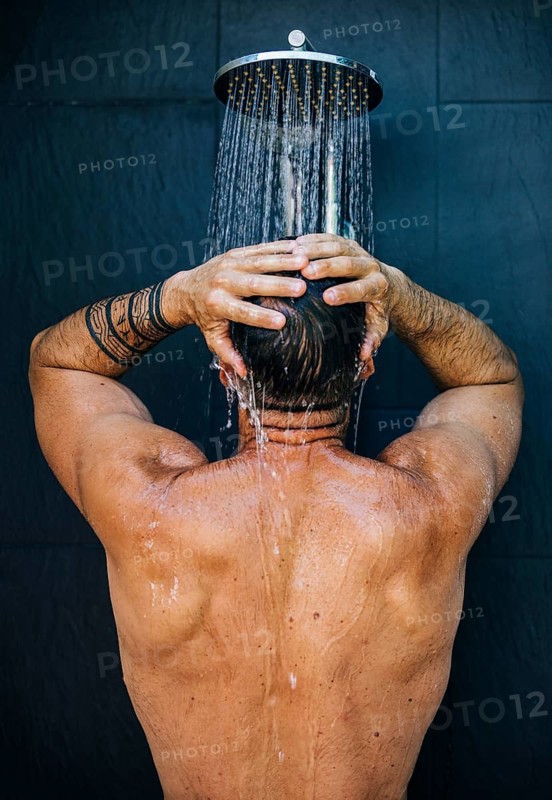 A man with tattoos enjoys a refreshing shower, standing with his back to the camera. Water cascades from the shower head, creating a relaxing and rejuvenating scene