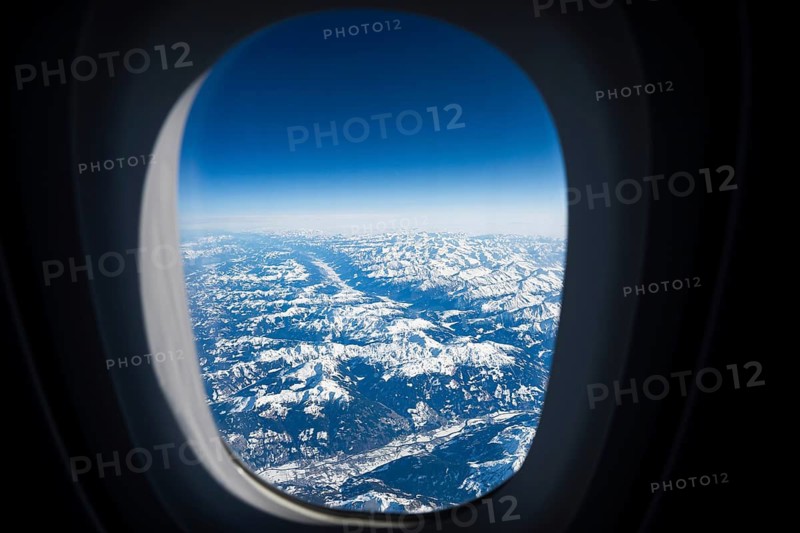 Spectacular aerial view of snow-capped mountain peaks and deep valleys seen through a commercial airplane window during a winter flight in Europe