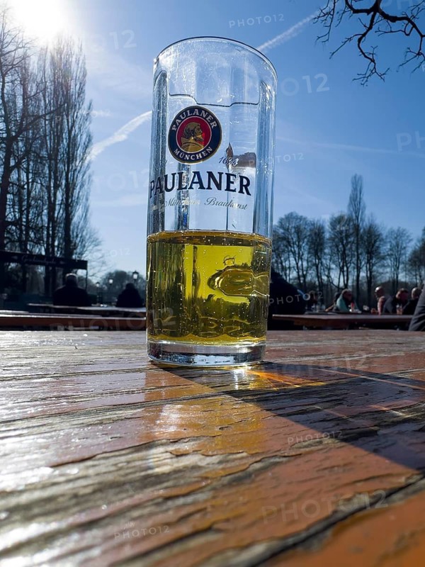 Half-filled Paulaner beer glass on a weathered beer garden table, behind it beer garden visitors, Kleinhesseloher See, Munich, Bavaria, Germany
