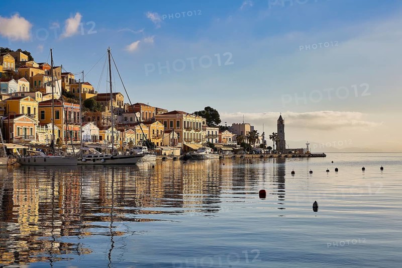 Lively harbour town with buildings reflecting in the water and a lighthouse. Tranquil Mediterranean atmosphere, Symi Town, Symi, Dodecanese, Greek Islands, Greece