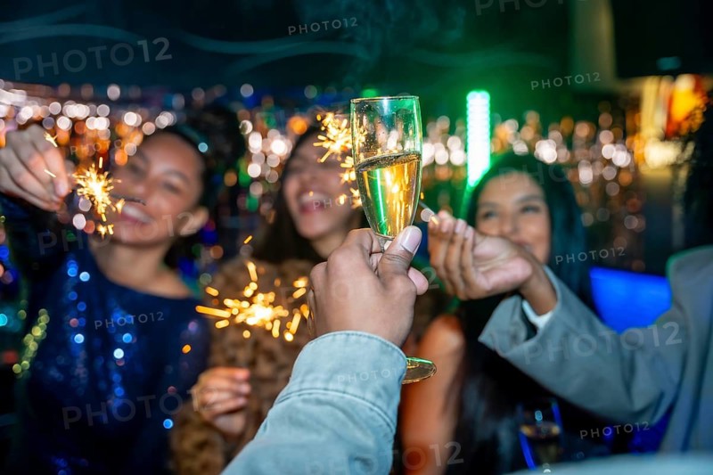 Group of diverse young adult friends toasting with champagne glasses and holding sparklers while enjoying a vibrant night party, celebrating success, and having fun together