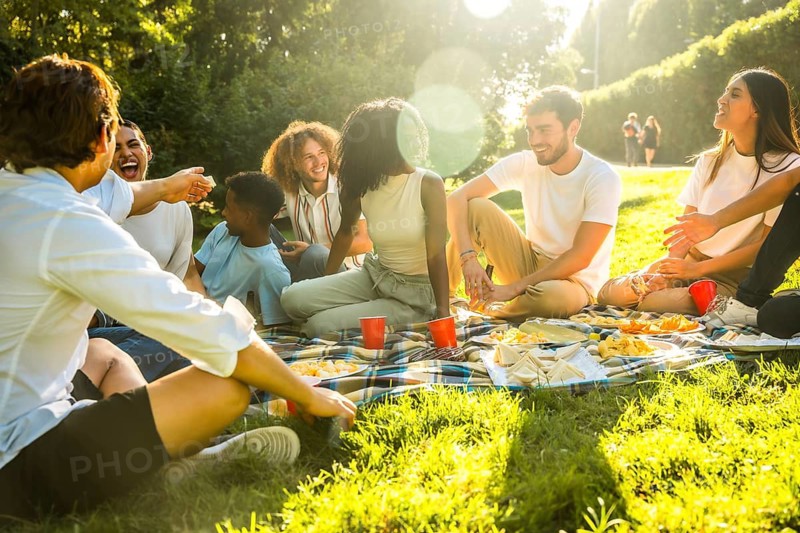 Rays of the sun illuminating multi-ethnic friends sitting on blanket enjoying a picnic in a park