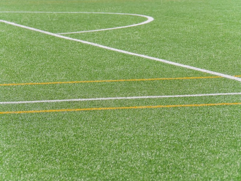A high quality image showing a close up view of white and yellow lines on an artificial grass soccer field, capturing the vibrant colors and clear markings typical of soccer grounds and its textures