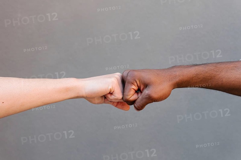 Close-up of two hands exchanging a fist bump against a neutral background, symbolizing unity, friendship, and teamwork across diversity and cultural boundaries