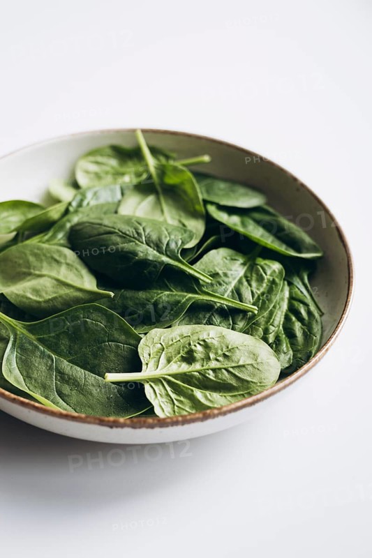 A top view of fresh green spinach leaves in a ceramic bowl placed on a white background. The vibrant spinach leaves offer a natural, healthy food theme, ideal for culinary uses