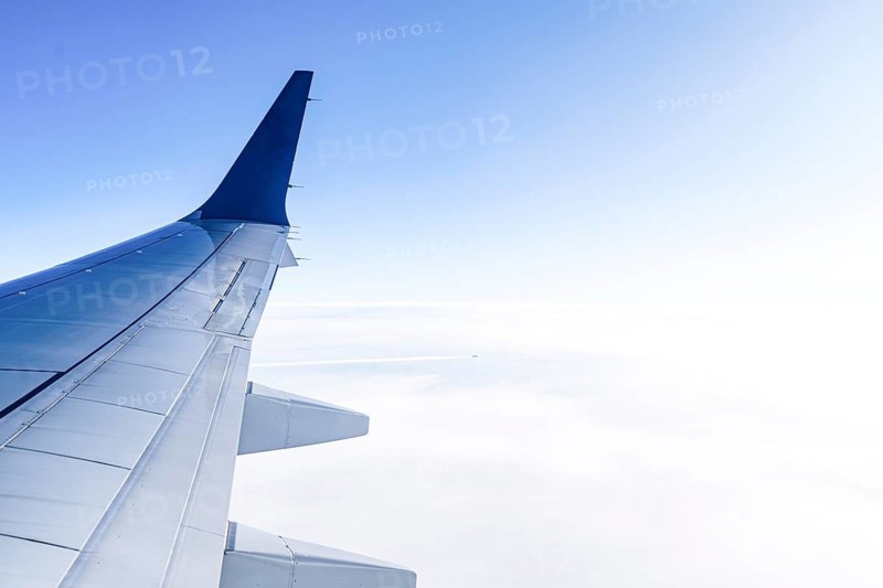 A view from an airplane window showcasing a blue sky and fluffy clouds below. The airplane wing is prominently visible, creating a sense of travel and adventure