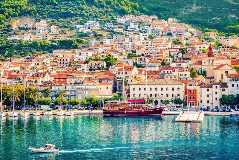 Aerial view Colorful waterfront of Makarska on the Adriatic Sea, Croatia. Sailboats and a red yacht in the marina below Biokovo mountains—sunny summer travel destination