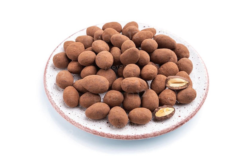 Almond in chocolate dragees on ceramic plate isolated on white background. Side view, close up