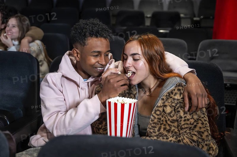 Young couple enjoys a movie date, sharing popcorn and a tender moment in the darkened theater
