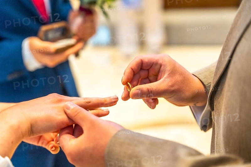 A man is giving a ring to a woman. The man is wearing a suit and the woman is wearing a wedding ring