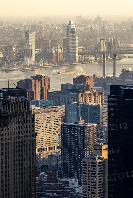 Top view of New York City at sunset, capturing the golden light casting over the buildings, river, and bridges. Stunning urban landscape with a warm glow