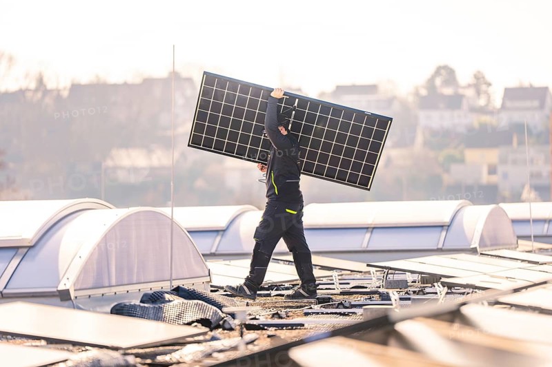Worker lifts a solar panel on a roof in an urban area in sunny weather, PV installation at OBI Baumarkt, Mühlacker, Enzkreis, Germany