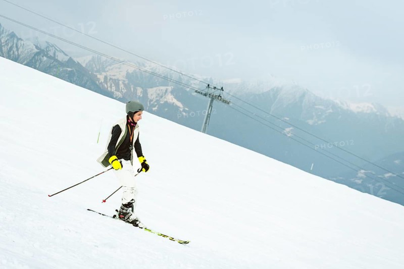 Georgian skier boy teenager skiing alone on snowy beginner slope with ski lift chairs passing above at Gudauri ski resort in Caucasus mountains Georgia