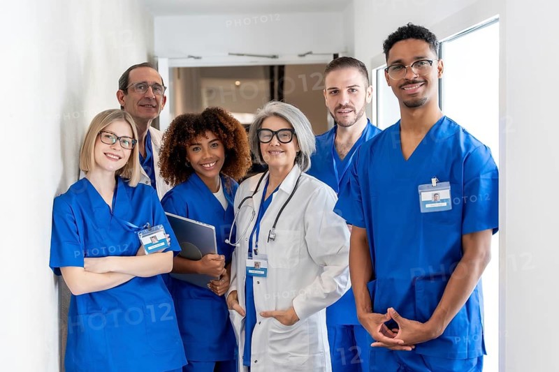 Diverse team of doctors and nurses in scrubs and lab coats standing in a bright hospital hallway, smiling confidently to convey teamwork, care and professional trust