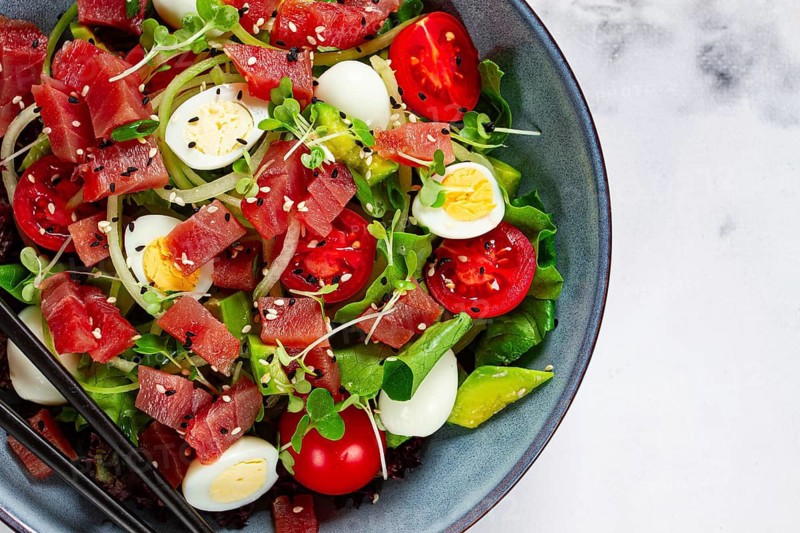 Salad with fresh tuna, cherry tomatoes and quail eggs and avacado, served with chopsticks