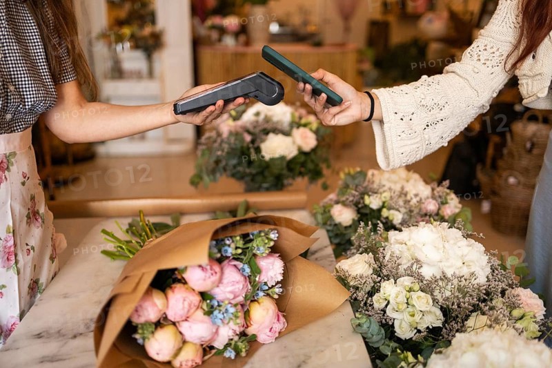 Women in a florist business use contactless payment on mobile devices surrounded by an assortment of colorful flower bouquets, exemplifying modern retail technology