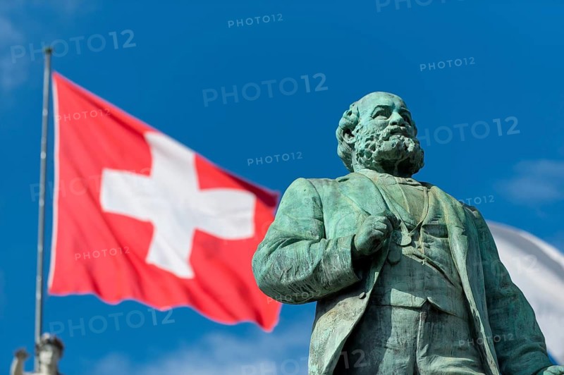 Swiss flag behind monument to Alfred Escher, Swiss politician, business leader and railway pioneer, by Richard Kissling, Bahnhofplatz central railway station, Zurich, Canton of Zurich, Switzerland