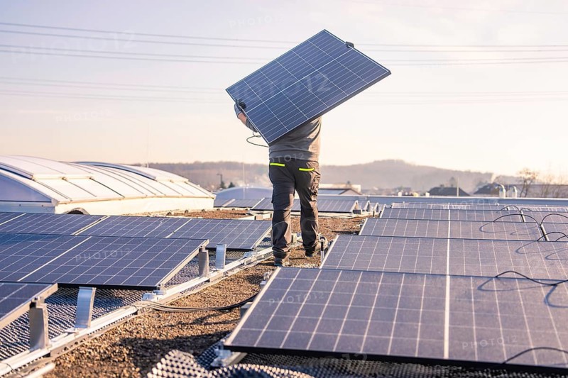 A worker stands with a solar panel on a roof surrounded by landscape, PV installation at OBI Baumarkt, Mühlacker, Enzkreis, Germany