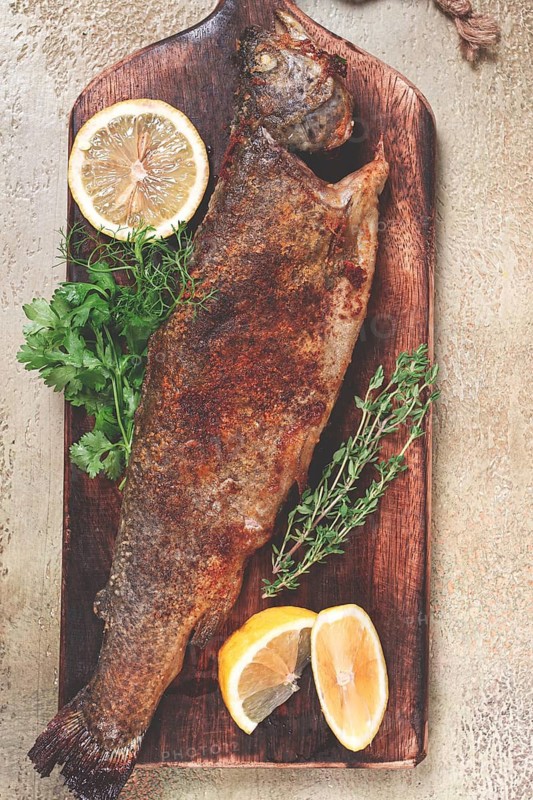 Fried rainbow trout, with herbs and citrus fruits, on a wooden chopping board, top view