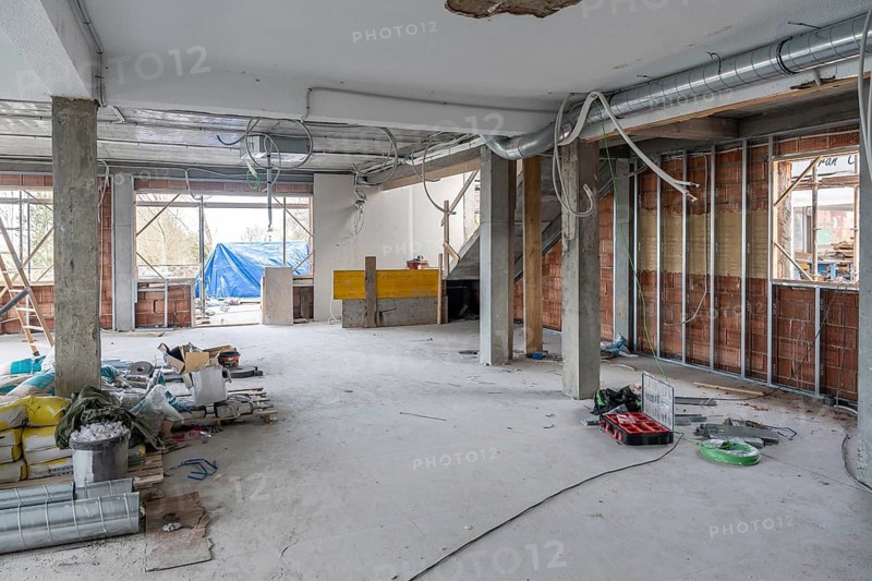 Indoor commercial space under renovation featuring concrete pillars, new brick walls with metal studs, exposed wiring, and air conditioning ducts being installed, indicating ongoing development