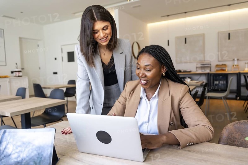 Two businesswomen collaborating on a laptop, enjoying the convenience of working remotely in a hotel lobby during their business trip