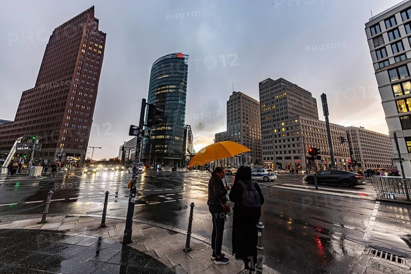 Potsdamer Platz Berlin in the evening with traffic on the streets. When it rains, the skyscrapers are reflected in puddles of water. People traveling with umbrellas. Berlin, Germany