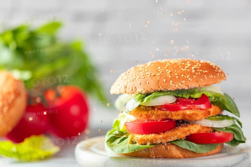 Sesame falls on burgers with vegan schnitzel, tomatoes, onions and salad with ingredients in the background