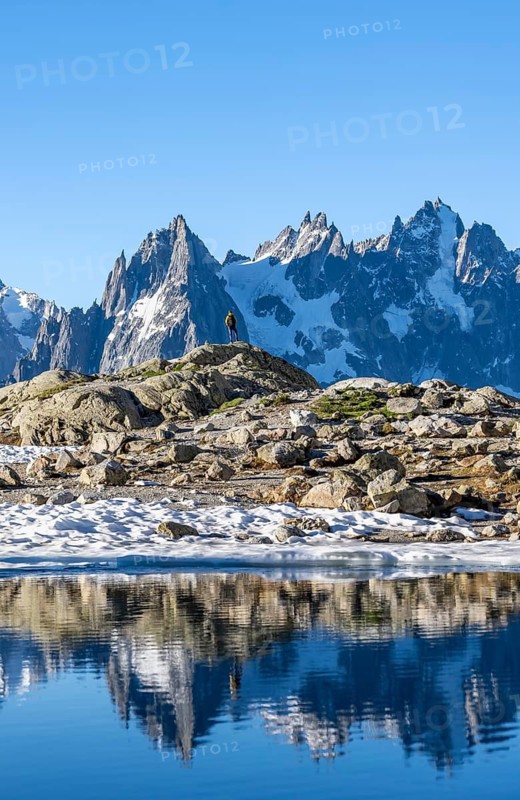 Young man in front of impressive mountain landscape in morning light, reflection in the Lac Blanc mountain lake, mountain summit, Aiguille Verte, Grandes Jorasses, Aiguille du Moine, Mont Blanc, Mont Blanc Massif, Chamonix-Mont-Blanc, Haute-Savoie, France